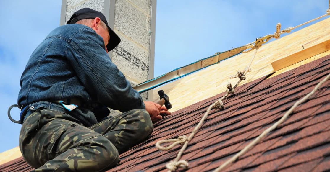 Roofer nailing asphalt shingles beside the metal flashing near a roof edge